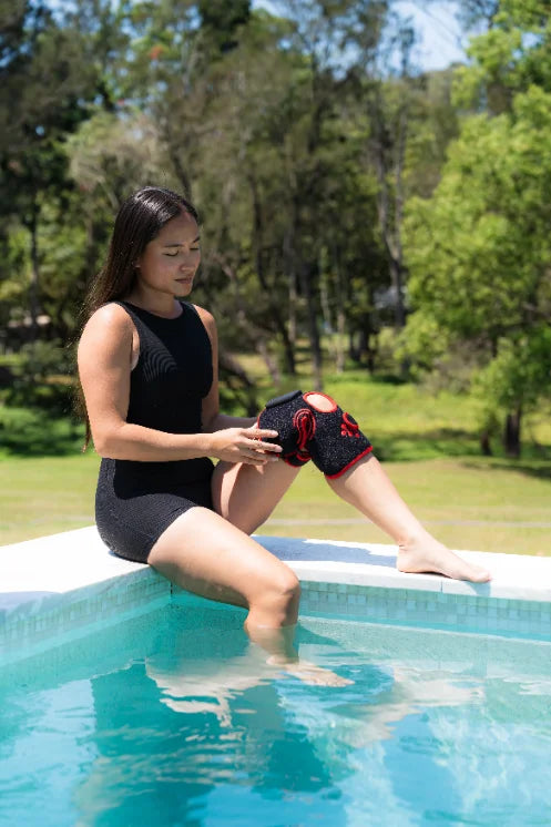 Woman seated beside a swimming pool wearing an Infraredi joint wrap on her raised knee.