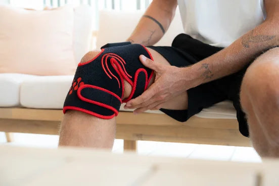 Man adjusting an Infraredi joint wrap around his knee while seated on a sofa.
