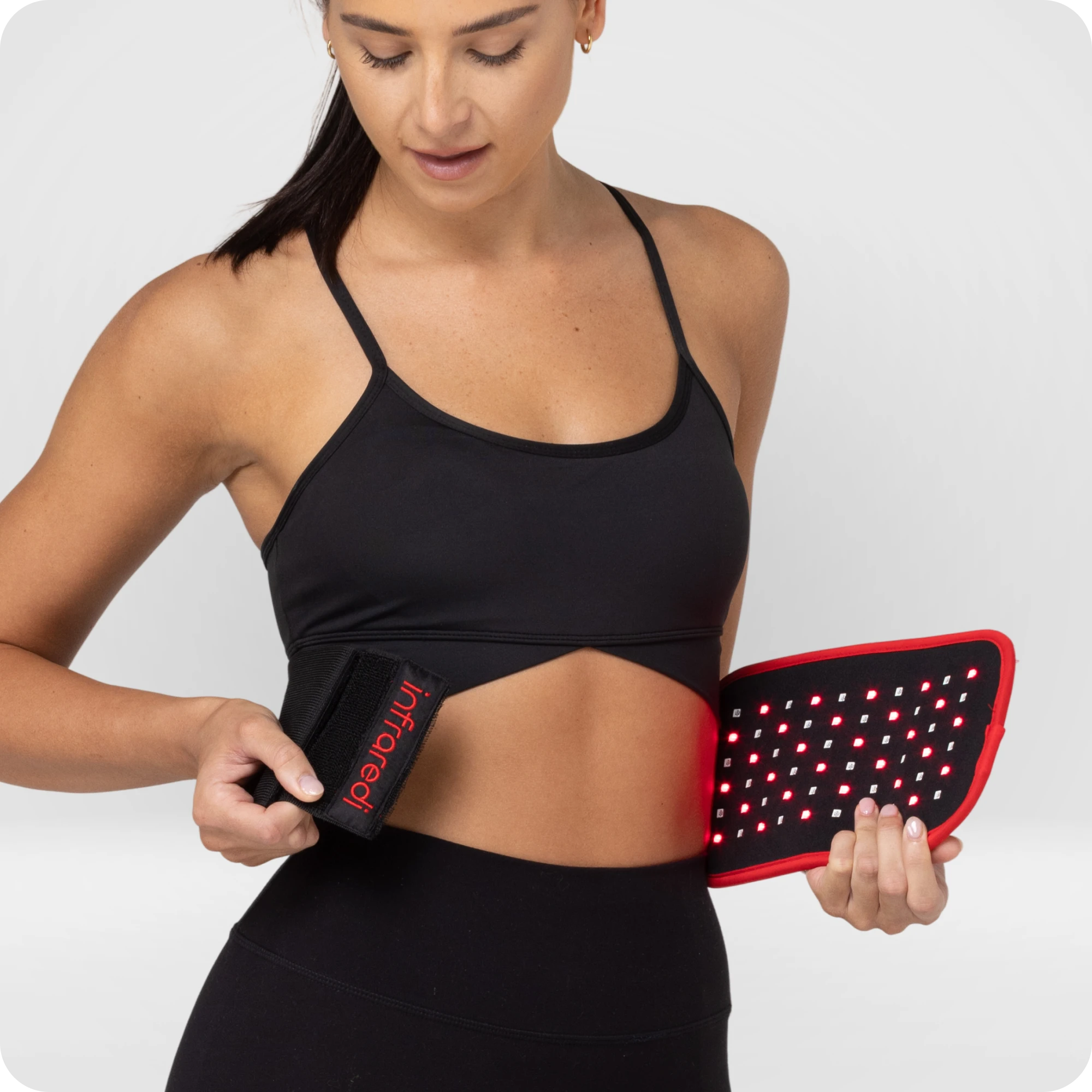 Woman positioning an illuminated Infraredi Body Wrap against her bare waist.